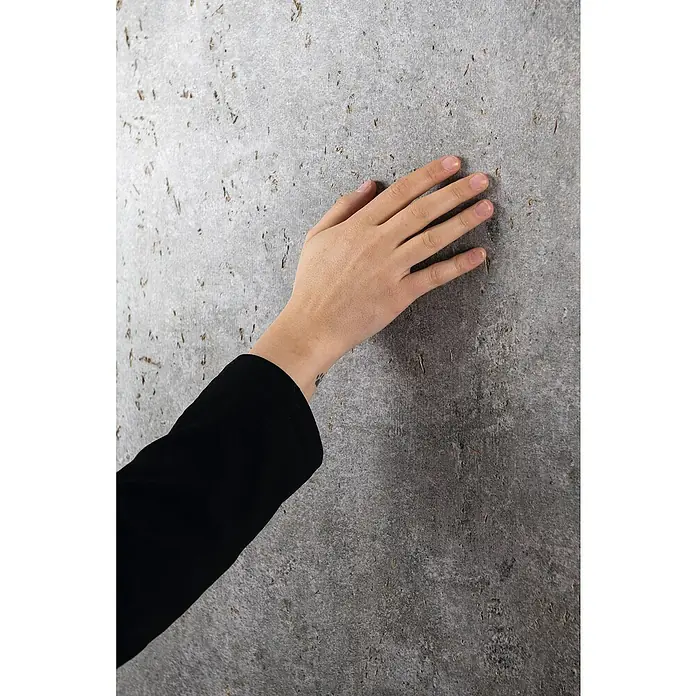 Egger Wandpaneel DecoWall - Rovigo Beton, 125 cm x 66 cm x 12 mm - Hand berührt eine strukturierte, graue Wand und zeigt die Textur und die Oberfläche.