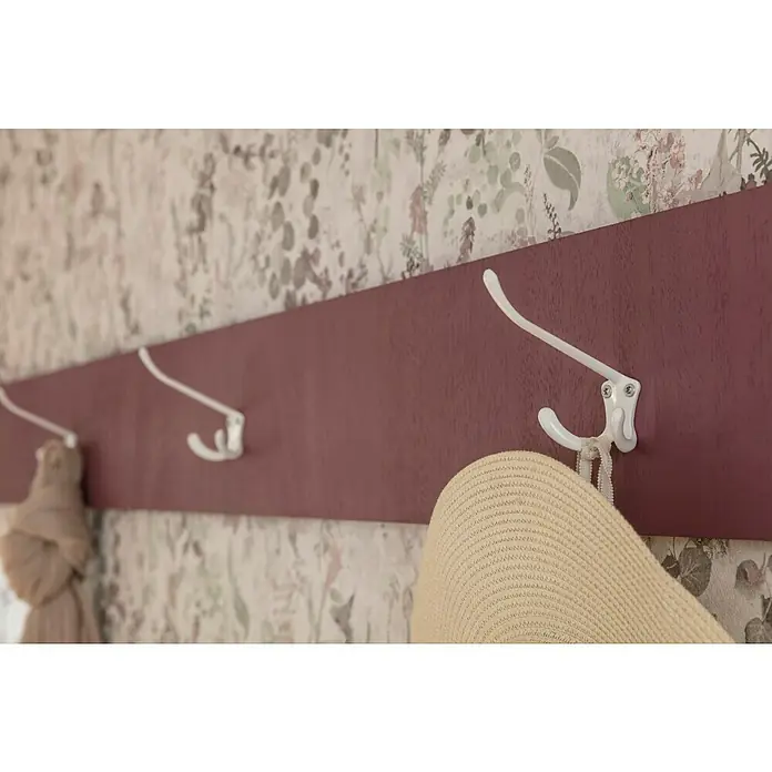 Häfele Gancho para colgar - Aluminio, Blanco, Montaje en la pared - Primer plano de un perchero de pared con ganchos blancos que sostienen un sombrero y una bufanda, sobre un papel tapiz floral.