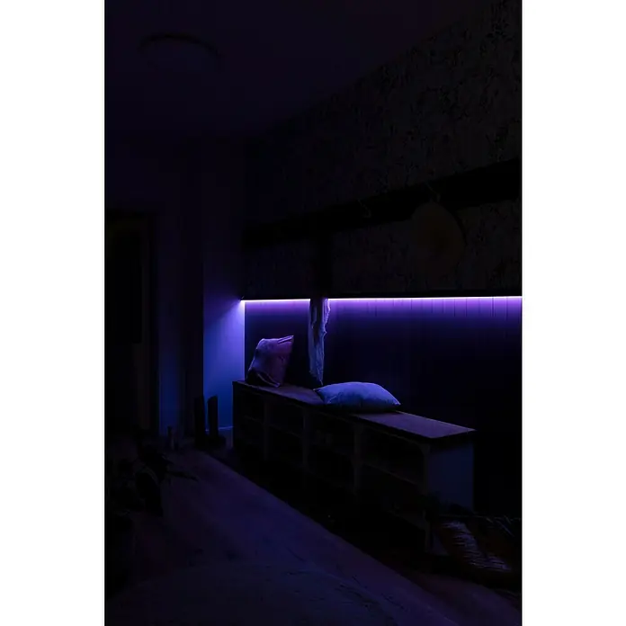 Nmc Decoflair Zierprofil CL13 - L x B x H: 2 m x 18 mm x 55 mm, Hochverdichtetes extrudiertes Polymer (HDPS) - Eindunkelungsbild eines Flurs mit einer Bank, die von einer violetten Lichtleiste beleuchtet wird, wodurch eine moderne und stimmungsvolle Atmosphäre entsteht.