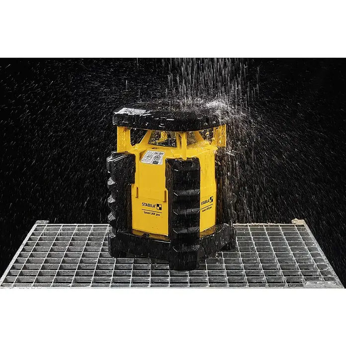 Stabila Rotationslaser LAR 300 - 7 -tlg. - Nahaufnahme eines Stabila Laser LAR 300 Rotationslasers im Regen auf einem Metallgitter, der die Widerstandsfähigkeit des Geräts hervorhebt.