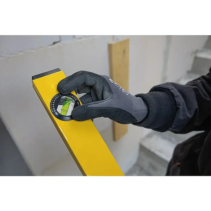 Stabila Wasserwaage Type 70 W - Länge: 100 cm, Anzahl Libellen: 2 Stk. - Nahaufnahme einer gelben Wasserwaage mit einer Hand, die sie an einer Wand hält, um ein genaues Ausrichten bei Bauarbeiten zu gewährleisten.