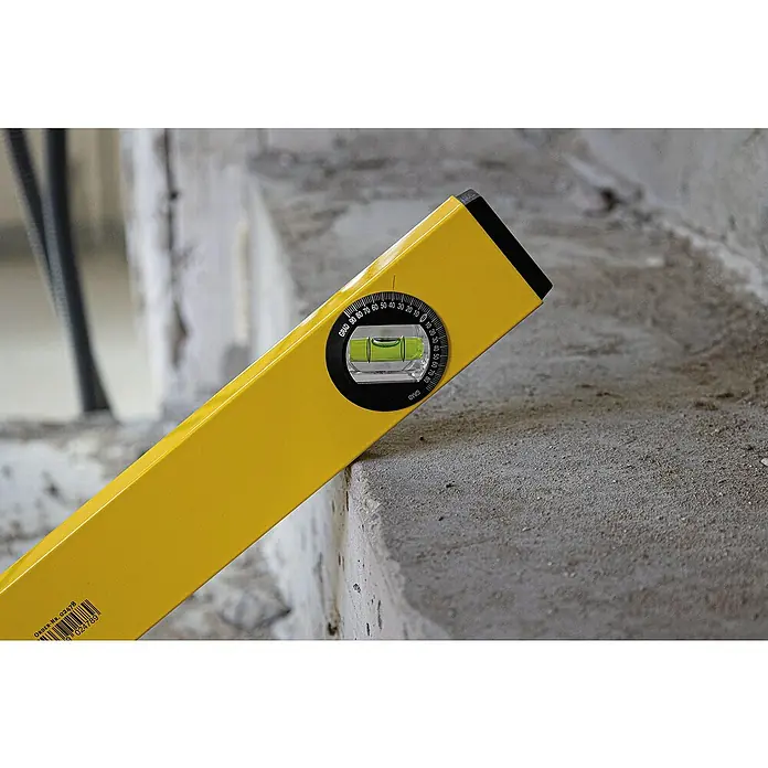 Stabila Wasserwaage Type 70 W - Länge: 100 cm, Anzahl Libellen: 2 Stk. - Nahaufnahme einer gelben Wasserwaage, die auf einer grauen Betonoberfläche liegt und die Neigung misst, mit einem gut sichtbaren Messgerät.