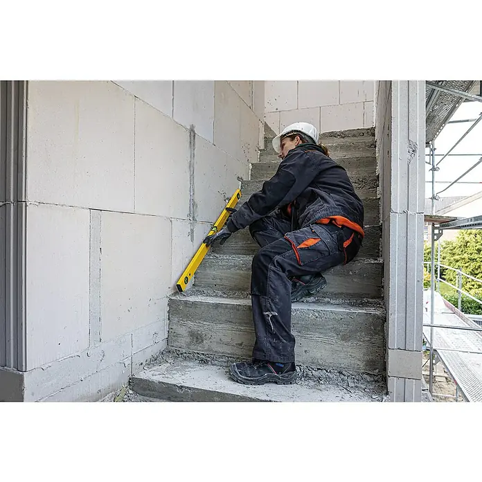 Stabila Wasserwaage Type 70 W - Länge: 100 cm, Anzahl Libellen: 2 Stk. - Bauarbeiterin prüft mit einer gelben Wasserwaage die Ausrichtung einer Mauer auf einer Baustelle, um Präzision zu gewährleisten.