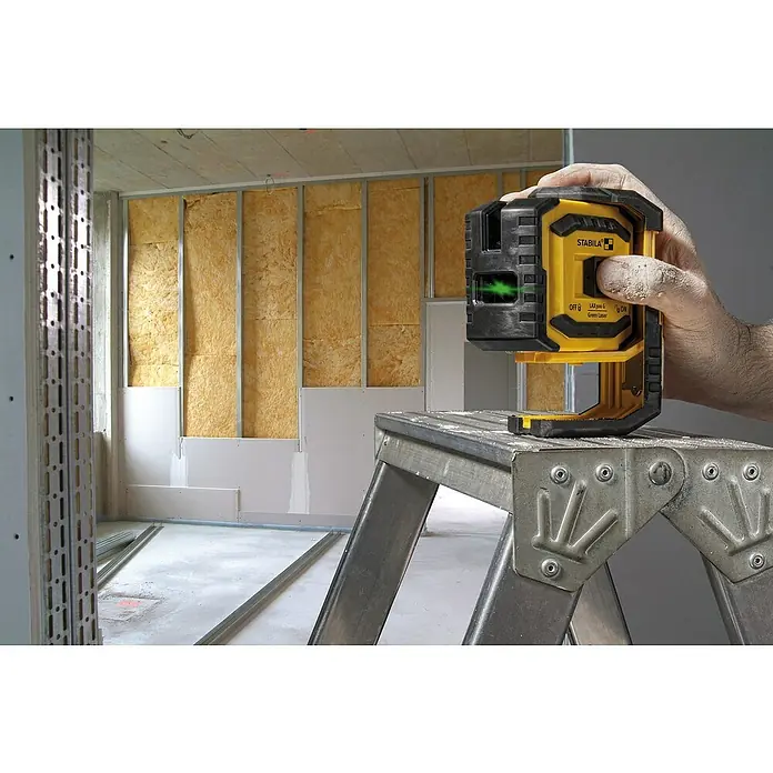 Stabila Kreuzlinienlaser LAX 300 G - Max. Arbeitsbereich: 30 m, 7 -tlg. - Ein gelber Stabila LAX300 G Linienlaser auf einer silbernen Trittleiter in einem unfertigen Raum.