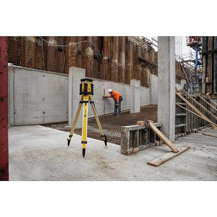 Stabila Rotationslaser LAR 35013 -tlg. - Baustellenansicht mit einem gelben Stabila-Laser-Nivelliergerät auf einem Stativ, das auf einer Betonfläche steht. Ein Arbeiter misst eine Wand im Hintergrund.