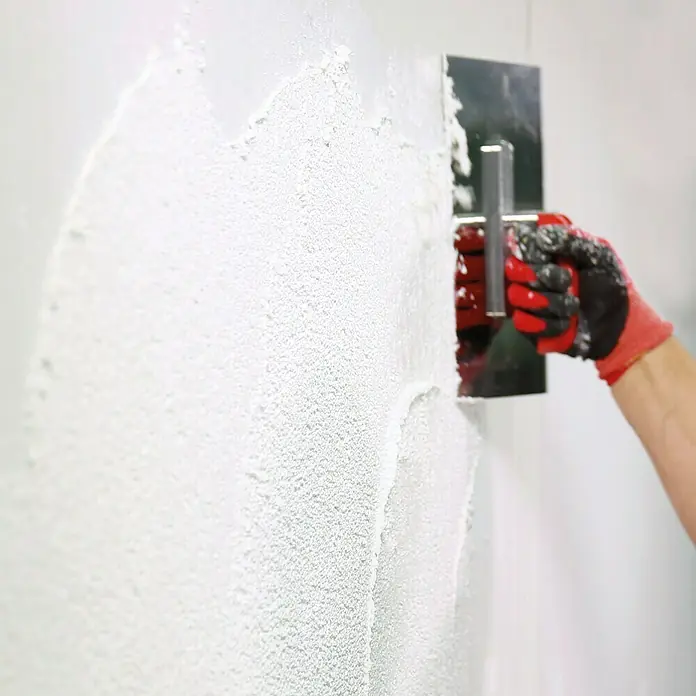 SG Weber Scheibenputz - Körnung: 3 mm, 25 kg - Verputzen einer Wand mit einem Spachtel und Handschuhen für Renovierungsarbeiten. Präzises Auftragen von Putz.