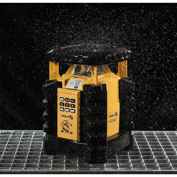 Stabila Rotationslaser LAR 35013 -tlg. - Das Bild zeigt einen gelben Stabila LAR 350 Baulaser, der auf einem Gitterrost steht und von Wasser bespritzt wird.