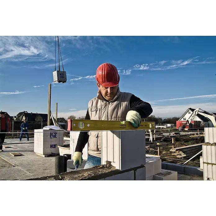 Stabila Wasserwaage Type 96-2Länge: 61 cm, Anzahl Libellen: 3 Stk. - Ein Bauarbeiter mit rotem Helm verwendet eine Wasserwaage auf einer Baustelle, um sicherzustellen, dass die Porenbetonsteine eben sind.