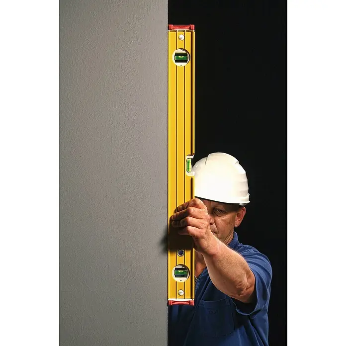 Stabila Wasserwaage Type 96-2Länge: 61 cm, Anzahl Libellen: 3 Stk. - Ein Bauarbeiter prüft mit einer gelben Wasserwaage die Ausrichtung einer grauen Wand, um sicherzustellen, dass alles perfekt waagerecht ist.