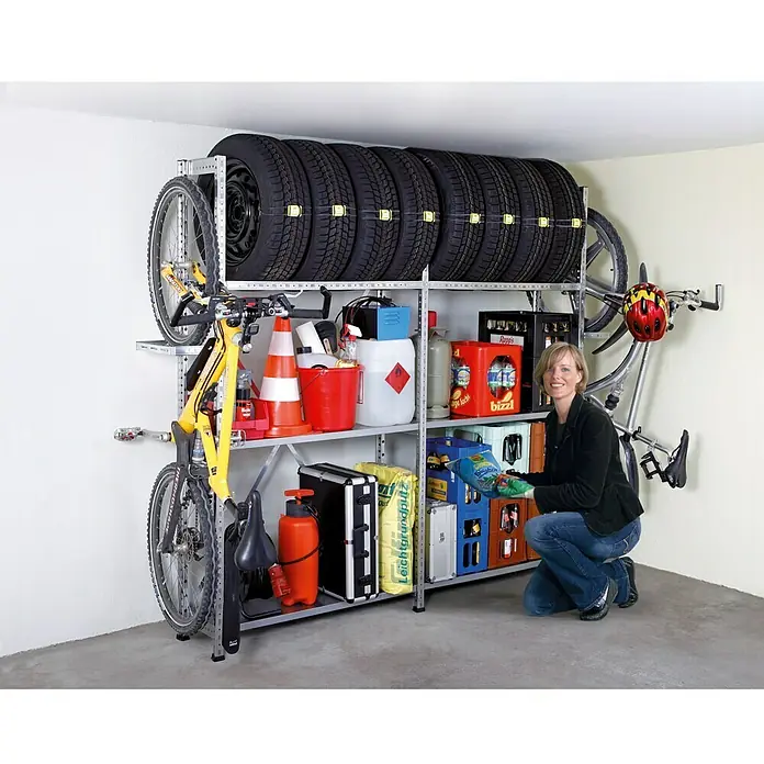 Scholz System Reifenträger-Set - Länge: 96 cm, Verzinkt, 2 Stk. - Garage mit einem Reifenregal, das Autoreifen, Fahrräder und Lagerkisten enthält, und einer Frau, die davor kniet.