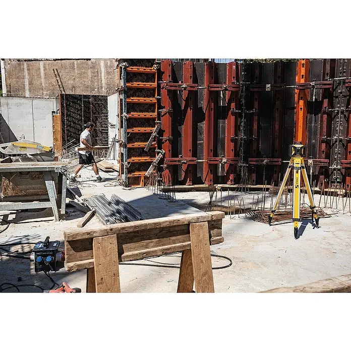 Stabila Rotationslaser LAR 160 - 9 -tlg. - Baustelle mit Bauholz, gelbem Nivelliergerät auf Stativ und einem Bauarbeiter, der Holz trägt.