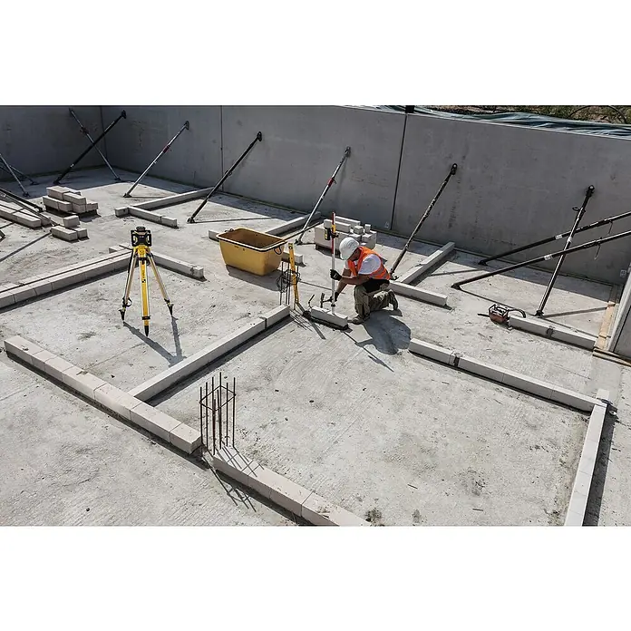 Stabila Rotationslaser LAR 160 - 9 -tlg. - Ein Bauarbeiter mit Schutzhelm und Warnweste arbeitet an der Fundamentlegung mit Nivelliergerät und Mauersteinen auf einer Baustelle.