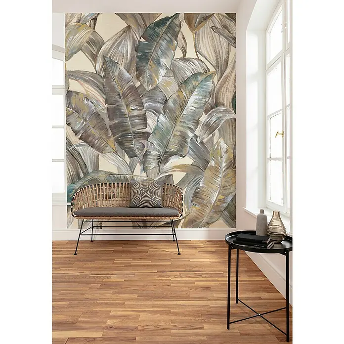 Komar Infinity 2 Fototapete Graceful Gold - B x H: 200 x 250 cm, Vlies - Ein Raum mit einer Bank und einem Beistelltisch vor einer Wand mit tropischen Blattmustern. Die Bank hat ein graues Kissen mit einem wirbelnden Design.