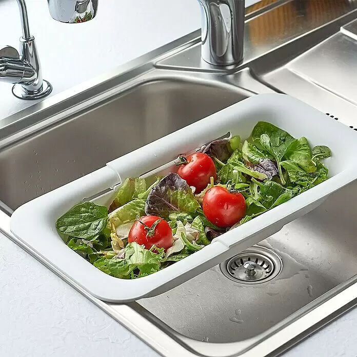 Zeller Present Spülbeckensieb - Weiß - Weißes ausziehbares Sieb über einer Edelstahlspüle mit frischem Salat und Tomaten.
