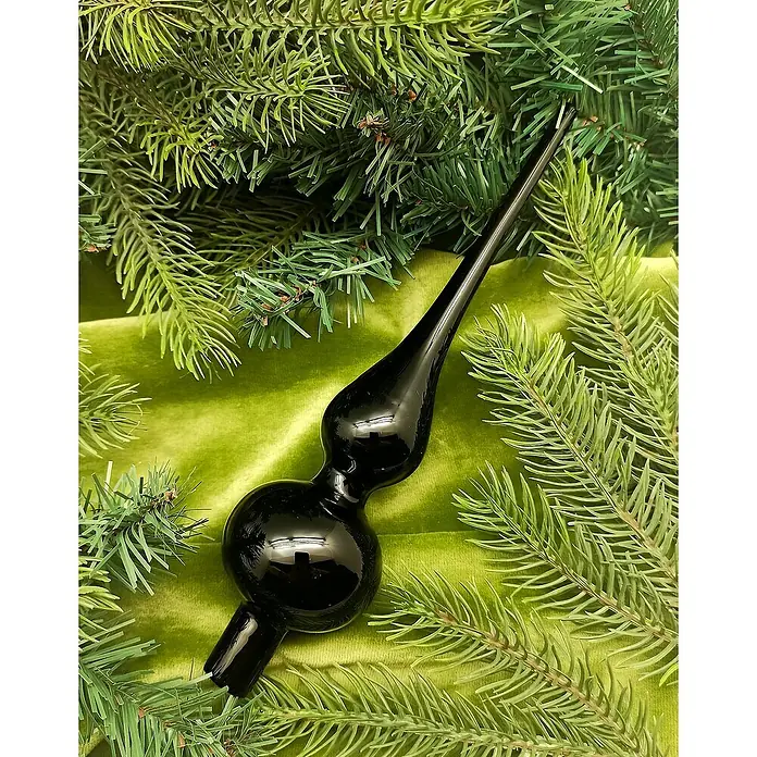 Christbaumspitze - Länge: 6,2 cm, Schwarz Opal - Nahaufnahme eines schwarzen Christbaumspitzes aus Glas, umgeben von Tannenzweigen und einem grünen Stoff. Elegante Weihnachtsdekoration.