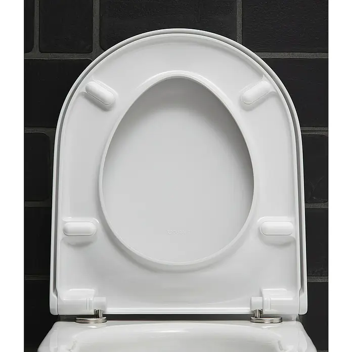 Duravit Starck 3 Wand-WC-Set - Spülrandlos, Mit antibakterieller Glasur, Spülform: Tief, WC Abgang: Waagerecht, Weiß - Nahaufnahme eines weißen WC-Sitzes mit einem modernen Design vor einem Hintergrund aus schwarzen Ziegeln.