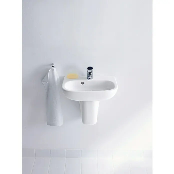 Duravit D-Code Waschbecken - 45 x 34 cm, Ohne Spezialglasur, Hahnloch: Mitte, Mit Überlauf, Weiß - Wandmontiertes Waschbecken mit Seife, Armatur und Handtuch vor einer weissen Wand und einem gefliesten Boden.