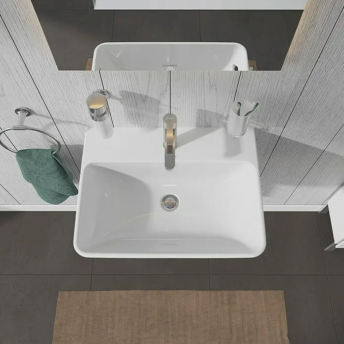 Duravit ME by Starck Waschtisch Typ 2 - 60 x 46 cm, Ohne Spezialglasur, Hahnloch: Mitte, Mit Überlauf, Weiß - Eine Aufsicht auf ein weißes Waschbecken mit Armatur, Seifenspender und Handtuchring in einem Badezimmer mit grauen Fliesen und einem Teppich.