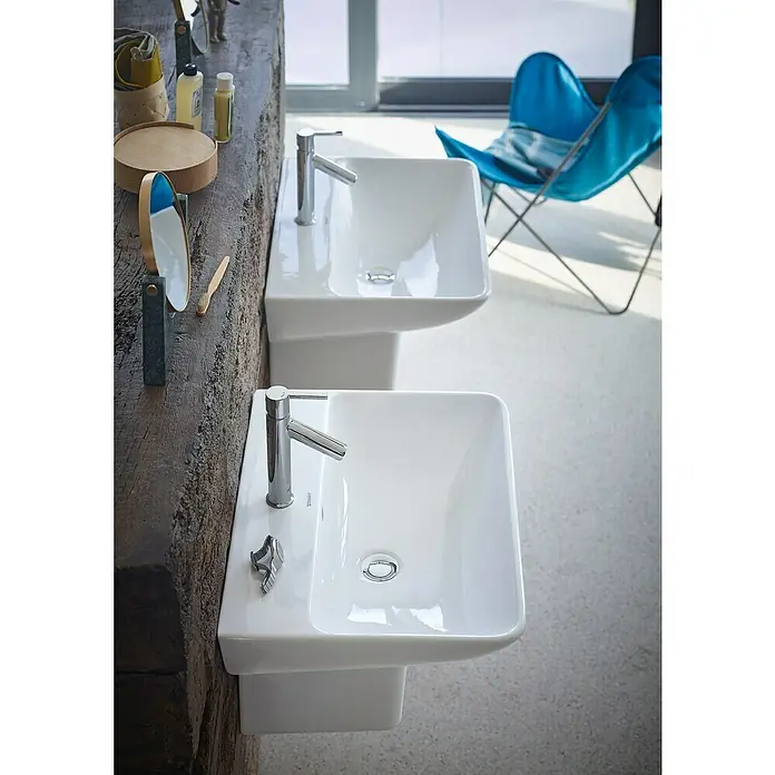 Duravit ME by Starck Waschtisch Typ 2 - 60 x 46 cm, Ohne Spezialglasur, Hahnloch: Mitte, Mit Überlauf, Weiß - Stilvolle Waschbecken im modernen Bad. Zwei Duravit Waschbecken mit Armaturen auf einem Holztisch, ergänzt durch einen Spiegel und eine blaue Sitzgelegenheit.