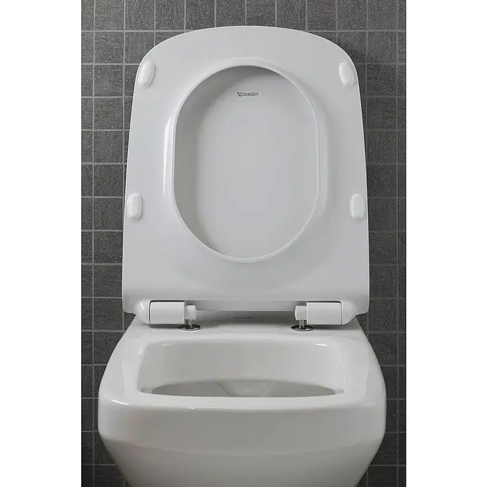 Duravit DuraStyle Wand-WC-Set - Spülrandlos, Ohne Spezialglasur, Spülform: Tief, WC Abgang: Waagerecht, Weiß - Detailaufnahme einer offenen, weißen Duravit Toilette vor einer grauen, gefliesten Wand.