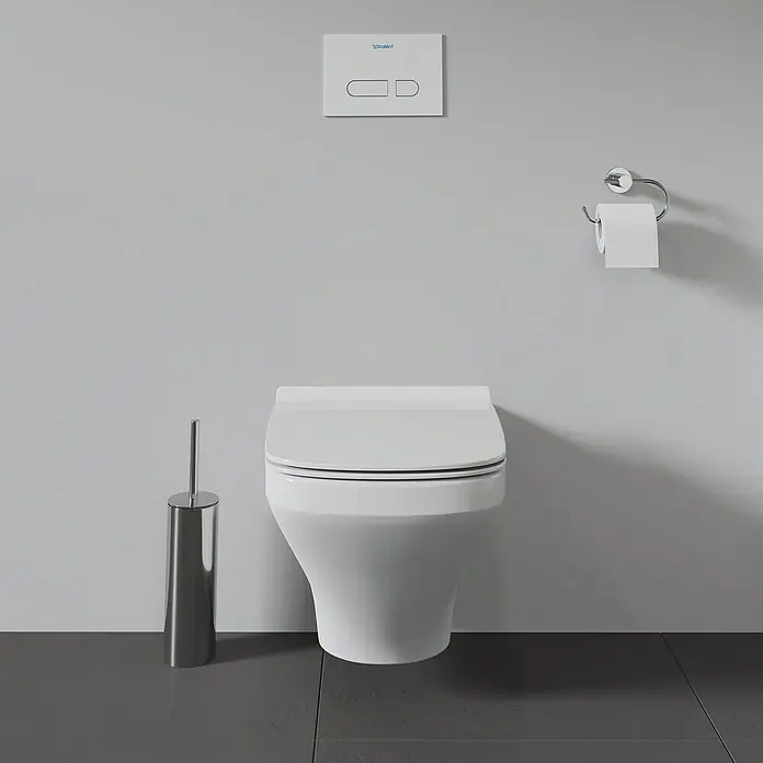 Duravit DuraStyle Wand-WC - Spülrandlos, Ohne Spezialglasur, Spülform: Tief, Sichtbarkeit Befestigung: Verdeckt, Weiß - Bild eines wandhängenden Duravit-WCs mit Toilettenbürste, Papierhalter und Betätigungsplatte vor einer grauen Wand.