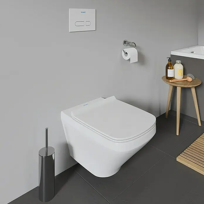 Duravit DuraStyle Wand-WC - Spülrandlos, Ohne Spezialglasur, Spülform: Tief, Sichtbarkeit Befestigung: Verdeckt, Weiß - Nahaufnahme einer modernen, wandhängenden Toilette mit Betätigungsplatte, Toilettenpapierhalter und einem kleinen Beistelltisch.