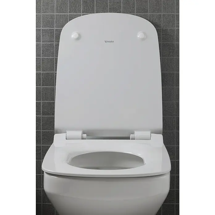 Duravit DuraStyle Wand-WC-Set - Spülrandlos, Ohne Spezialglasur, Spülform: Tief, WC Abgang: Waagerecht, Weiß - Nahaufnahme einer Duravit Toilette mit geöffnetem Deckel vor einer grauen, gefliesten Wand.