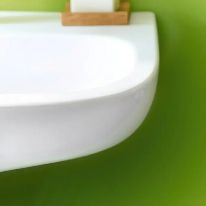 Duravit D-Code Waschtisch - 60 x 46 cm, Ohne Spezialglasur, Hahnloch: Mitte, Mit Überlauf, Weiß - Nahaufnahme eines modernen, weißen Waschbeckens an einer hellgrünen Wand, darüber eine hölzerne Seifenablage.