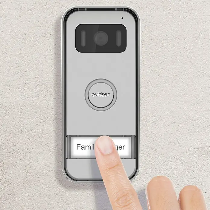 Avidsen Türklingel mit Kamera Prima kabelgebunden - Silber, 800 x 480 Pixel - Eine Avidsen-Türklingel mit Finger, der die Klingeltaste drückt. Das Gerät ist an einer Wand montiert und verfügt über eine Kamera.