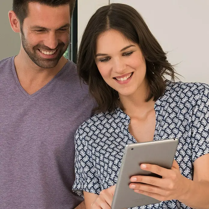 Philips WelcomeEye Farb-Video-Türsprechanlage Wireless - Bildschirmgröße: 7″, 1.920 x 1.080 Pixel (Full HD), Smarte Steuerung: Philips WelcomeEye App - Ein Paar schaut auf einem Tablet und lächelt. Das Tablet wird von der Frau gehalten, während der Mann daneben steht und zusieht.