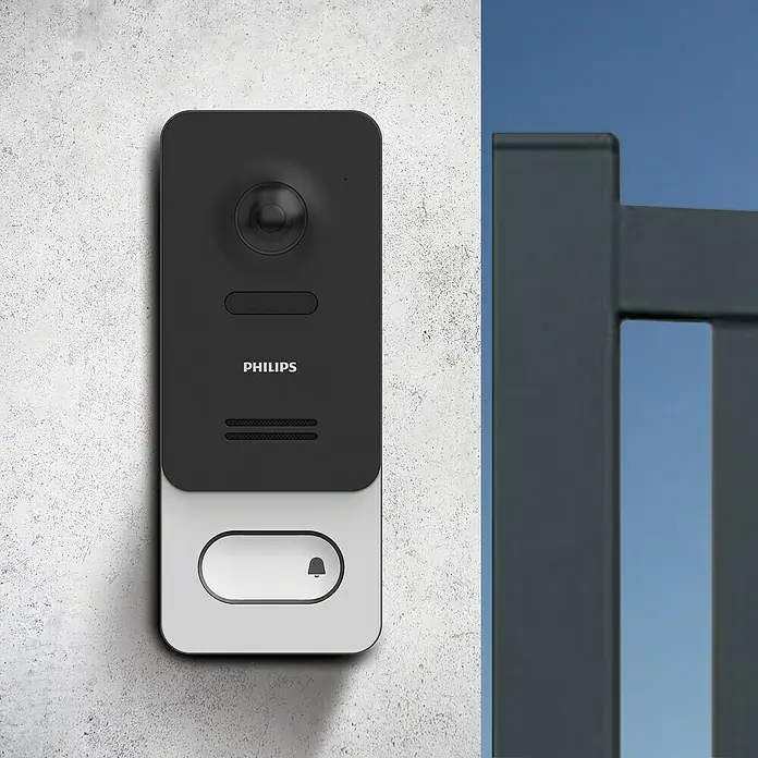 Philips WelcomeEye Farb-Video-Türsprechanlage Wireless - Bildschirmgröße: 7″, 1.920 x 1.080 Pixel (Full HD), Smarte Steuerung: Philips WelcomeEye App - Nahaufnahme einer Philips-Türklingel mit Videofunktion, montiert an einer Wand neben einem grauen Zaun.