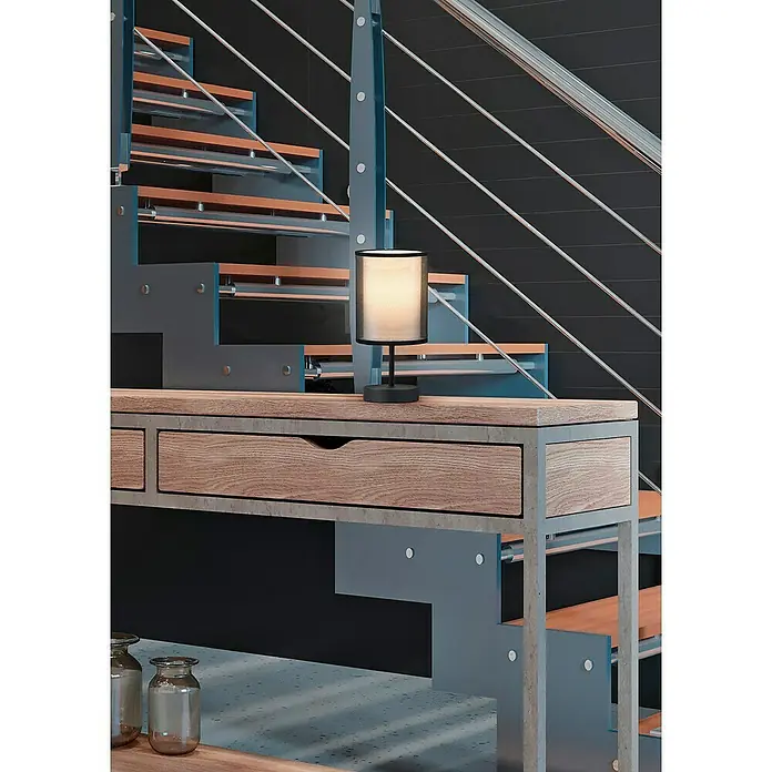 Trio Leuchten Burton Tischleuchte rund - 28 W, Ø x H: 12,5 x 28,5 cm, Schwarz-matt, E14 - Eine stilvolle Tischleuchte mit Stoffschirm auf einem Holzschreibtisch vor einer modernen Treppe.