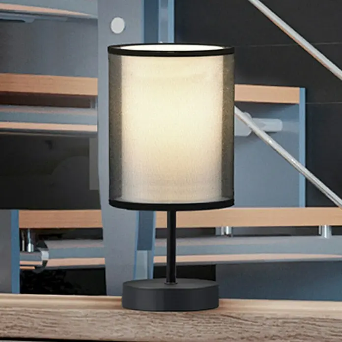 Trio Leuchten Burton Tischleuchte rund - 28 W, Ø x H: 12,5 x 28,5 cm, Schwarz-matt, E14 - Nahaufnahme einer stilvollen, modernen Tischlampe mit schwarzem Fuß und zylindrischem Schirm, die ein warmes Licht ausstrahlt.