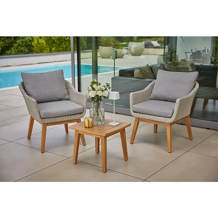 Sunfun Loungemöbel-Set Paula XL - 3 -tlg., Aluminium/Akazie/Polyrattan, Hellgrau/Braun - Gartenmöbel-Set mit zwei Stühlen und einem Tisch. Die Stühle sind aus Rattan und haben graue Kissen. Auf dem Tisch stehen Blumen und eine Lampe.
