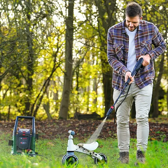 Bosch Universal Akku-Hochdruckreiniger UniversalAquatak 36V-100 - 8 -tlg., 36 V, 1 Akku - Ein Mann reinigt mit einem Bosch Hochdruckreiniger ein Kinderspielzeug im Garten, wobei der Fokus auf dem Bosch Produkt liegt.