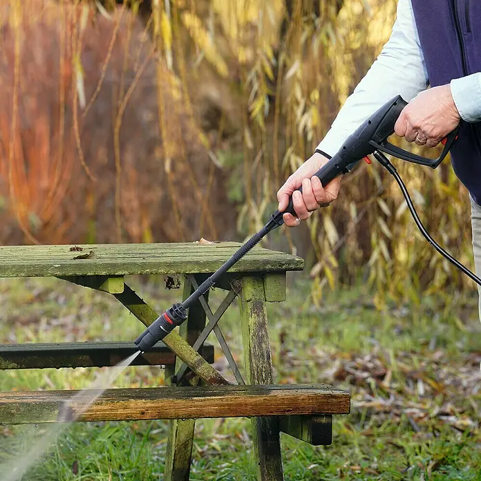 Bosch Universal Akku-Hochdruckreiniger UniversalAquatak 36V-100 - 8 -tlg., 36 V, 1 Akku - Der Hochdruckreiniger säubert eine alte, grüne Picknickbank im Freien und entfernt Schmutz und Ablagerungen mit kraftvollem Wasserstrahl.