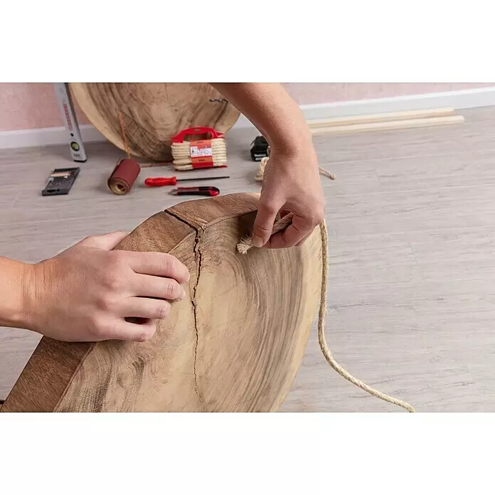 Stabilit Cuerda - 8 mm x 10 m, Materiales naturales - Manos enhebrando una cuerda de fibra natural a través de un orificio en una losa de madera redonda de color marrón claro, mostrando su veta y una grieta.