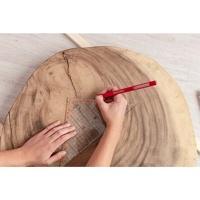 BAUHAUS Zimmermannsbleistift - Lindenholz, Länge: 240 mm - Ein Holztisch wird mit einem roten Bauhaus-Bleistift und einem transparenten Dreieck bearbeitet, um präzise Linien zu ziehen und das Design zu gestalten.