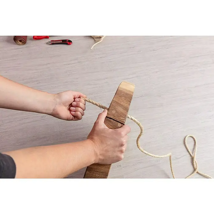 Stabilit Cuerda - 8 mm x 10 m, Materiales naturales - Primer plano de una persona enrollando una cuerda alrededor de un trozo de madera para un proyecto de bricolaje. Las herramientas están dispuestas al fondo.