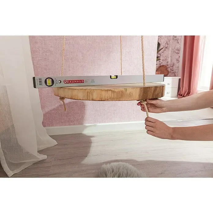Stabilit Sisalseil - 8 mm x 10 m, 3-schäftig gedreht - Nahaufnahme eines rustikalen, hängenden Baumstammtisches mit Nivellierwerkzeug zur Überprüfung der horizontalen Ausrichtung.