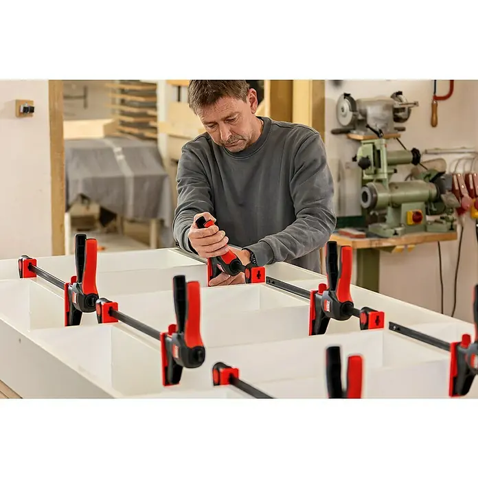 Bessey Einhandzwinge EZ 360-60 - Spannweite: 600 mm, Ausladung: 80 mm - Mann arbeitet mit einer Bessey Einhandzwinge an einem weißen Möbelstück in einer Werkstatt.\n
