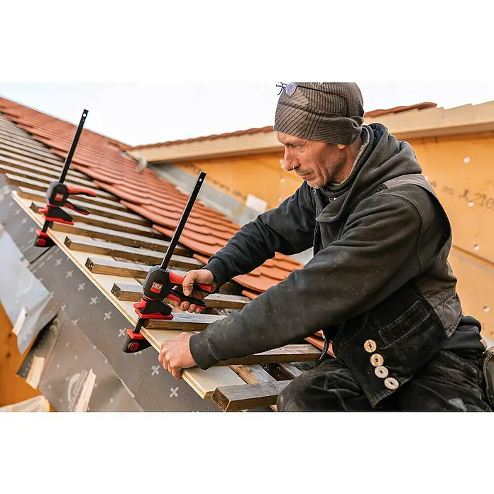 Bessey Einhandzwinge EZ 360-45 - Spannweite: 450 mm, Ausladung: 80 mm - Handwerker befestigt Holz mit einer BESSEY Einhandzwinge auf einem Dach. Die Zwinge ermöglicht einhändiges Spannen und ist ideal für Montagearbeiten.