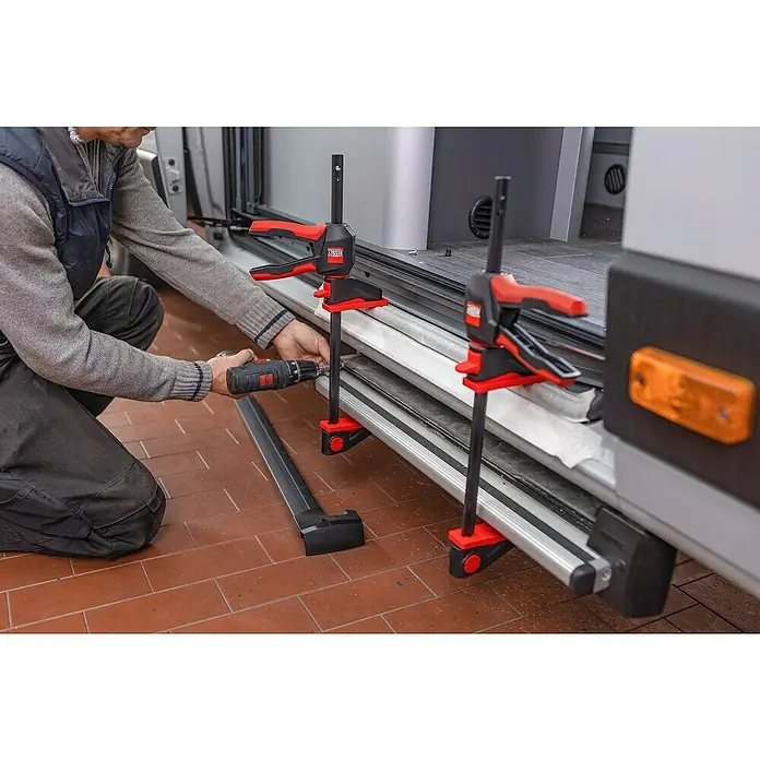 Bessey Einhandzwinge EZ 360-45 - Spannweite: 450 mm, Ausladung: 80 mm - Bild zeigt eine Person, die mit einem Akkuschrauber und BESSEY Hebelzwingen an einem Fahrzeug arbeitet, ideal für sicheres und präzises Fixieren.