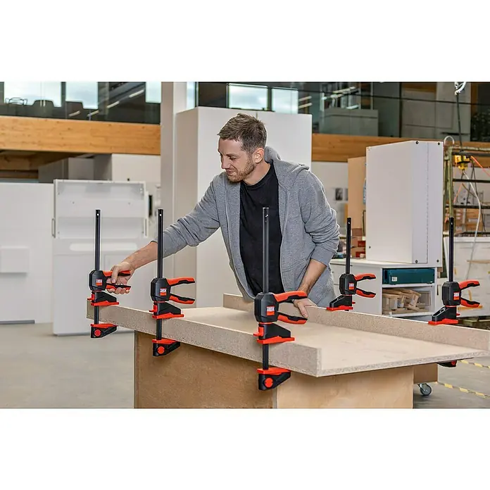 Bessey Einhandzwinge EZ 360-45 - Spannweite: 450 mm, Ausladung: 80 mm - Der Handwerker verwendet BESSEY Hebelzwingen, um Holzplatten zu fixieren. Die Zwingen sind rot und schwarz und stabilisieren das Werkstück.