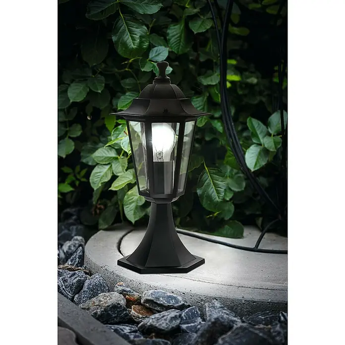 Eglo Laterna 4 Außenleuchte60 W, Schwarz, Ø x H: 19,5 x 38,5 cm - Elegante schwarze Außenleuchte mit Glühbirne auf einem Steinsockel vor üppigem Grün, die eine warme und einladende Atmosphäre schafft.