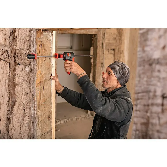 Bessey Einhandzwinge EZ 360-45 - Spannweite: 450 mm, Ausladung: 80 mm - Nahaufnahme eines Mannes mit Mütze, der einen Türrahmen mit einer roten und schwarzen Spreizzwinge befestigt, während er die Stabilität des Rahmens prüft.