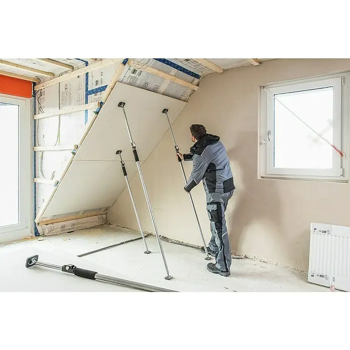 Bessey Montagestütze ST 125Verstellbar: 75 cm - 125 cm - Ein Bauarbeiter montiert eine Gipskartonplatte an einer Dachschräge mit Hilfe von Stützen, die das Material während der Installation halten.