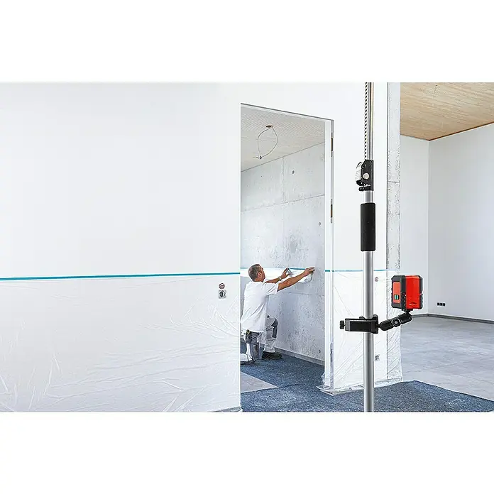 Bessey Klemmhalter STE-LH - Passend für: Geräte wie Laser mit einer 1/4“ Gewindeaufnahme - Ein Handwerker verwendet ein Linienlaser-Nivelliergerät, um präzise Markierungen für Malerarbeiten in einem Raum mit vorbereiteten Wänden zu setzen.