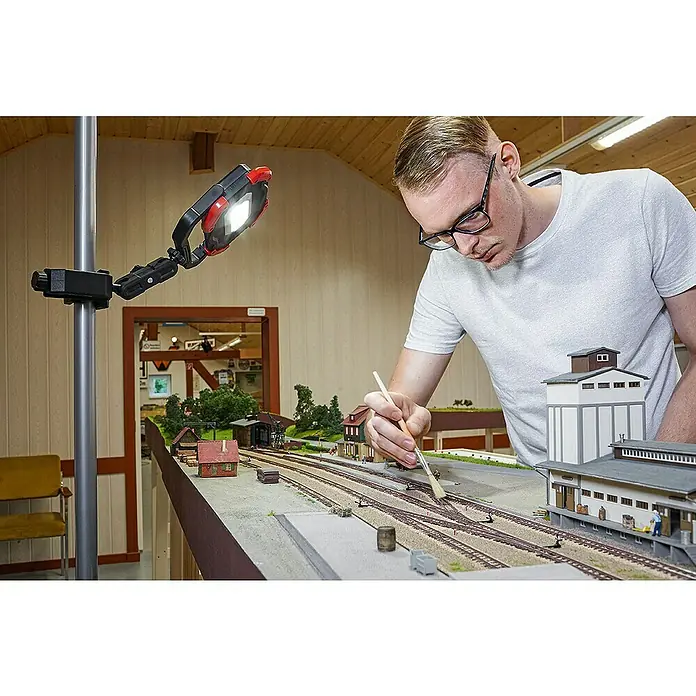 Bessey Klemmhalter STE-LH - Passend für: Geräte wie Laser mit einer 1/4“ Gewindeaufnahme - Mann arbeitet an einer Modelleisenbahn mit einer Arbeitsleuchte, die auf einem Stativ montiert ist, um präzise Details zu bearbeiten.
