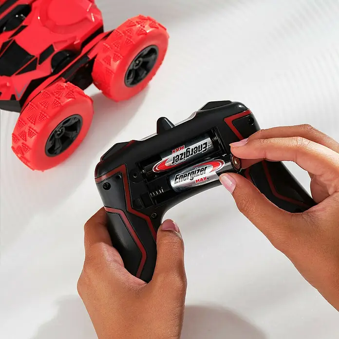 Energizer Max Batterie - Micro AAA, 1,5 V, Alkali-Mangan, 20 Stk. - Eine Nahaufnahme von Händen, die Batterien in eine schwarze Fernbedienung mit roter Akzentuierung neben einem roten Spielzeugauto einlegen.
